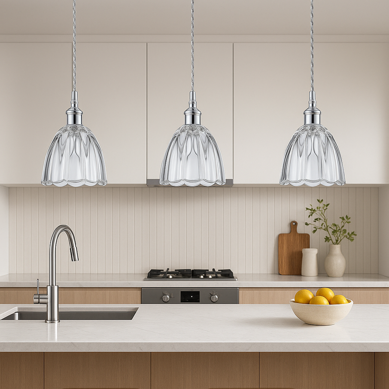 Modern kitchen with three glass pendant lights, a bowl of fruit on the counter, and a cutting board.