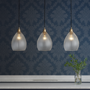Three pendant lights hanging above a counter with yellow stools against a blue patterned wall.