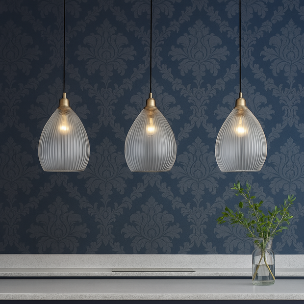 Three pendant lights hanging above a counter with yellow stools against a blue patterned wall.