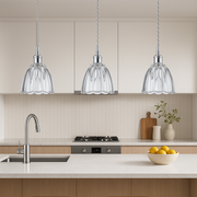Modern kitchen with three glass pendant lights, a bowl of fruit on the counter, and a cutting board.