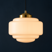 Pendant light with beige glass shade and gold fixture on a black background