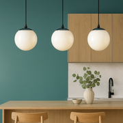 Modern kitchen with wooden counter, stools, and pendant lights against a teal wall.