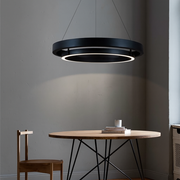 Modern black pendant light hanging above a wooden table with books and a candle.