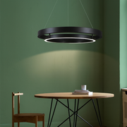 Black circular pendant light hanging above a wooden table and chair against a green wall.