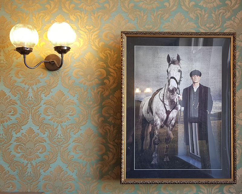 Framed portrait of a person with a horse on a patterned wall.