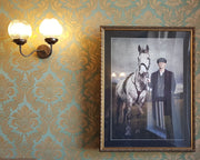 Framed portrait of a person with a horse on a patterned wall.